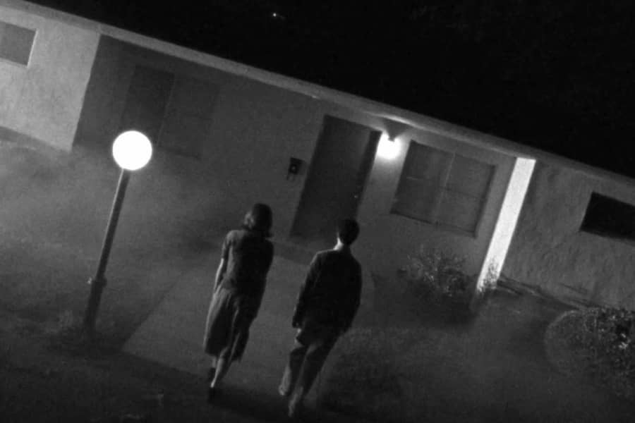 a man and woman approach a house on a foggy night