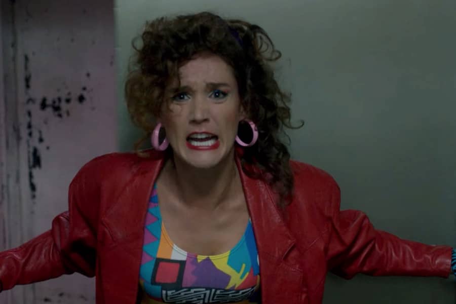 80s teen girl in brightly colored clothes screams as she braces by an elevator