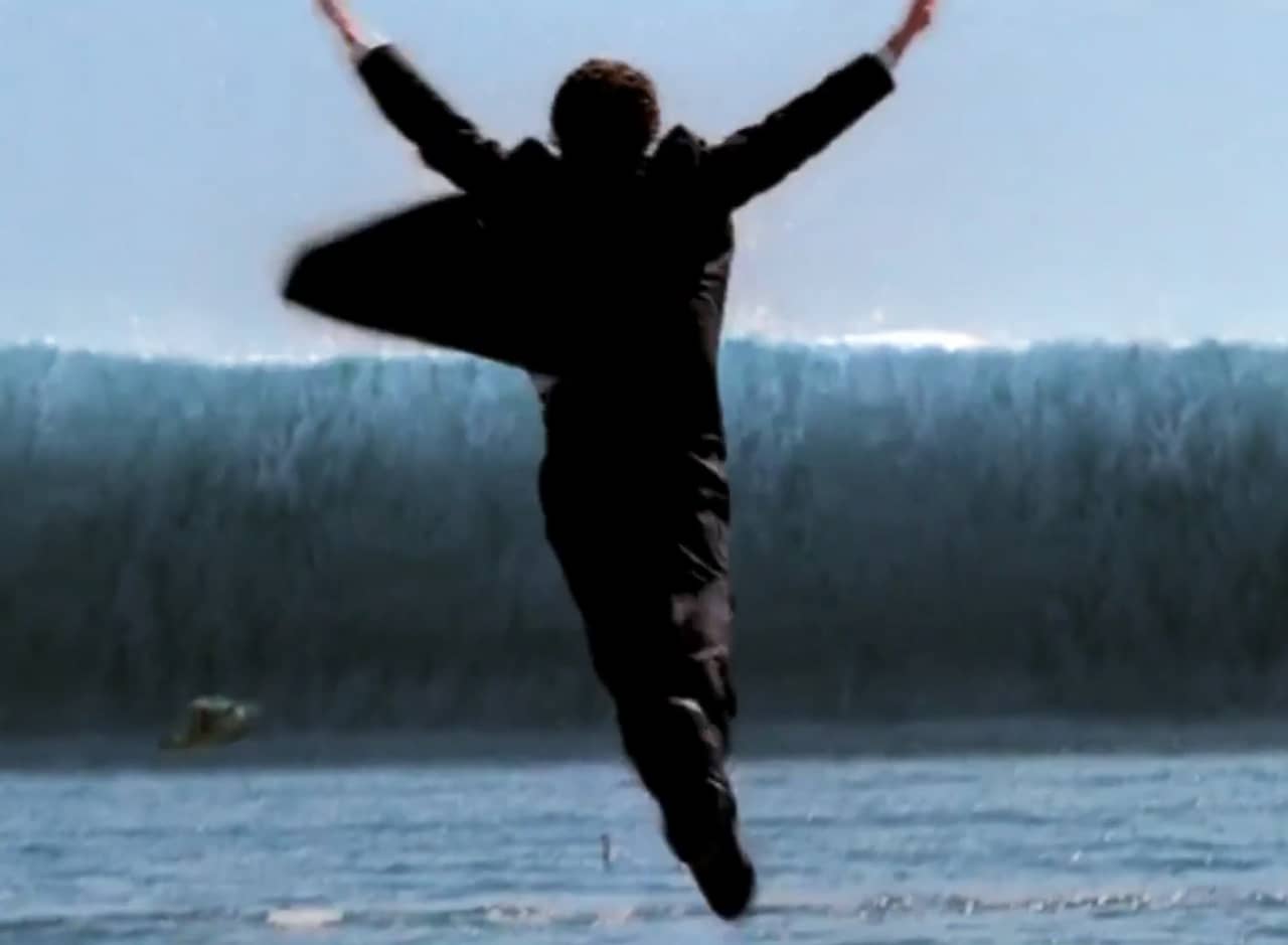 a man in a suit jumps into the ocean as a huge wave approaches