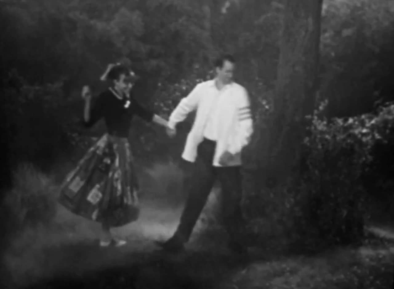 Billy and Sally Mae, a 50s teen couple, walk hand in hand through the woods