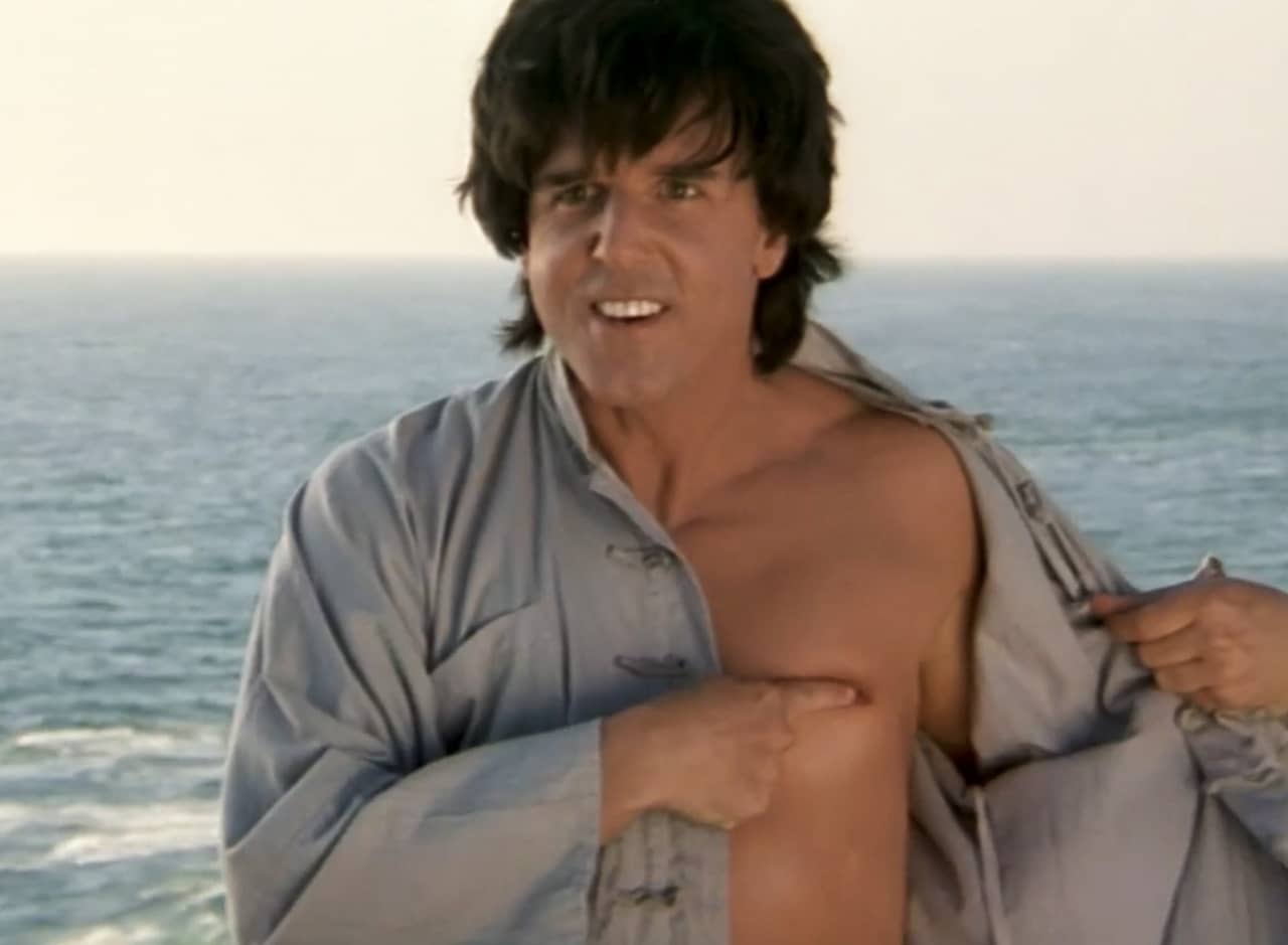 The Chosen One, on a cliff by the sea, opens his shirt to touch his nipple