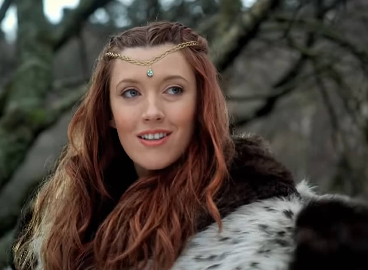 a red haired woman in the woods wearing a gem headpiece and a fur coat
