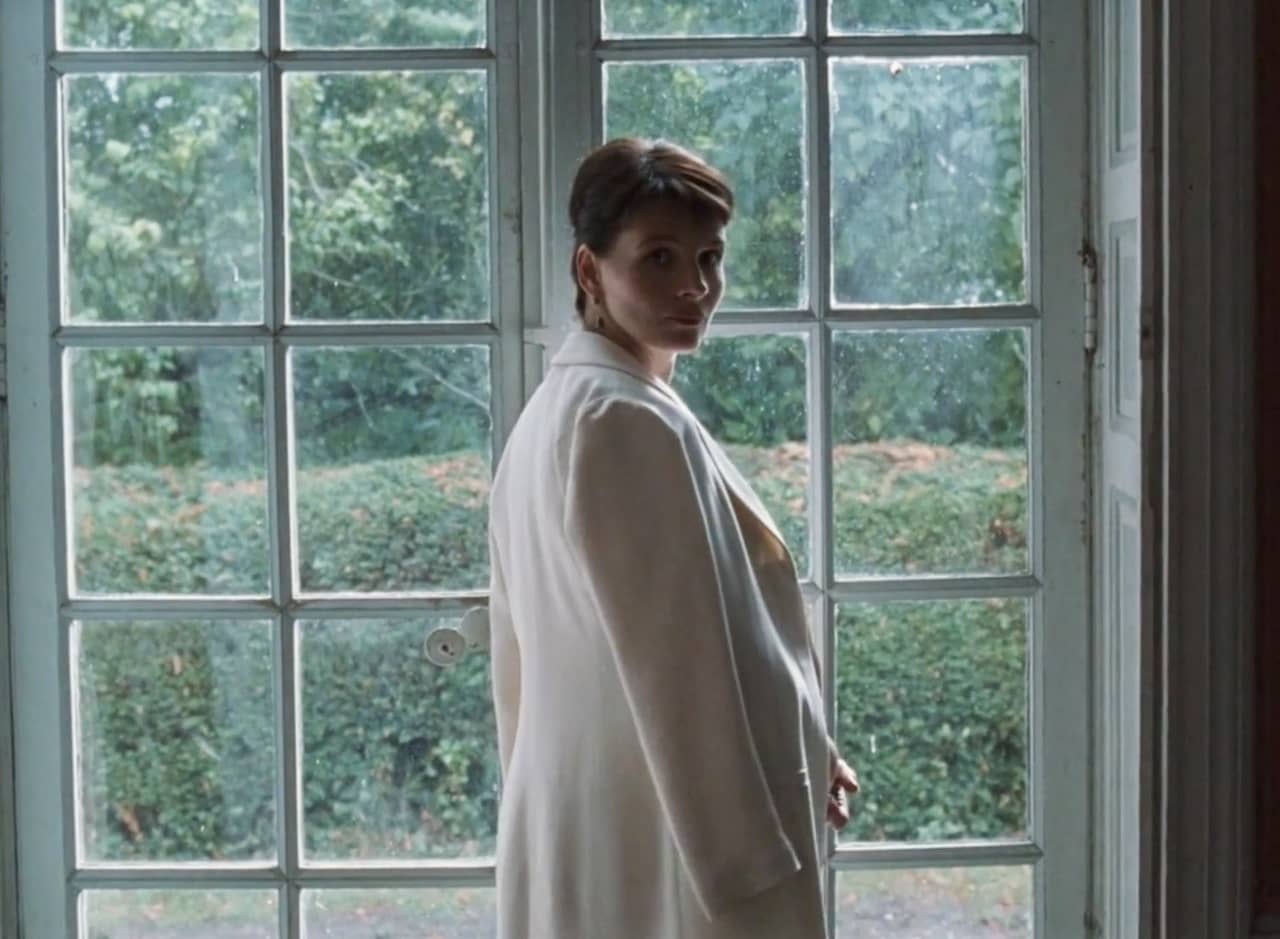 Anne Laurent in a white blazer looks back at the camera in front of a large window