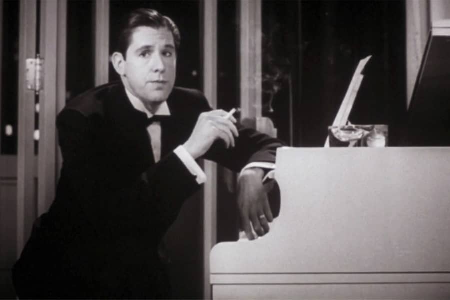 Henry dressed in a tuxedo smoking a cigarette at a grand piano