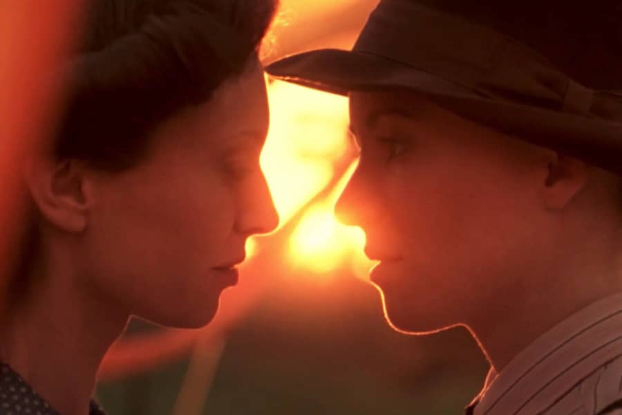 the two women face each other for a kiss, with the sun setting in the background