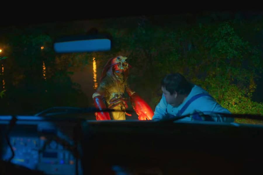 the huge lobster approaches a man, illuminated by his truck’s headlights