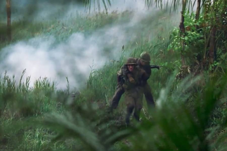 Billy carries Danny through the jungle as bombs explode