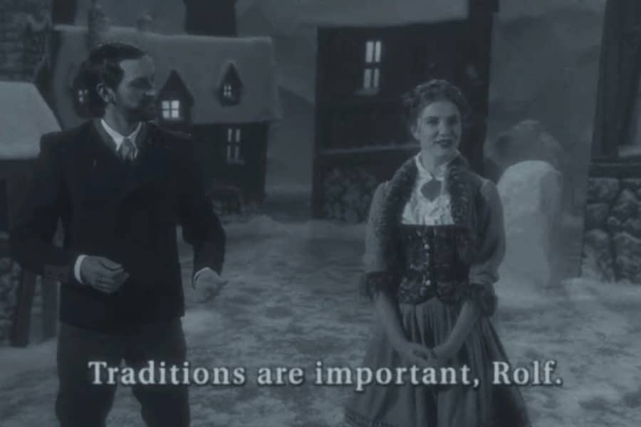 a man and woman, Rolf and Gerta, stand in a village square; subtitles read “Traditions are important, Rolf.”