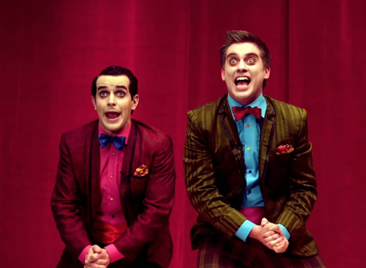 excited hosts in loud, colorful suits with bowties and pale face makeup