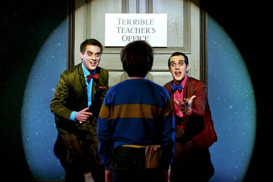 the hosts welcome the kid to a door labeled “Terrible teacher’s office”