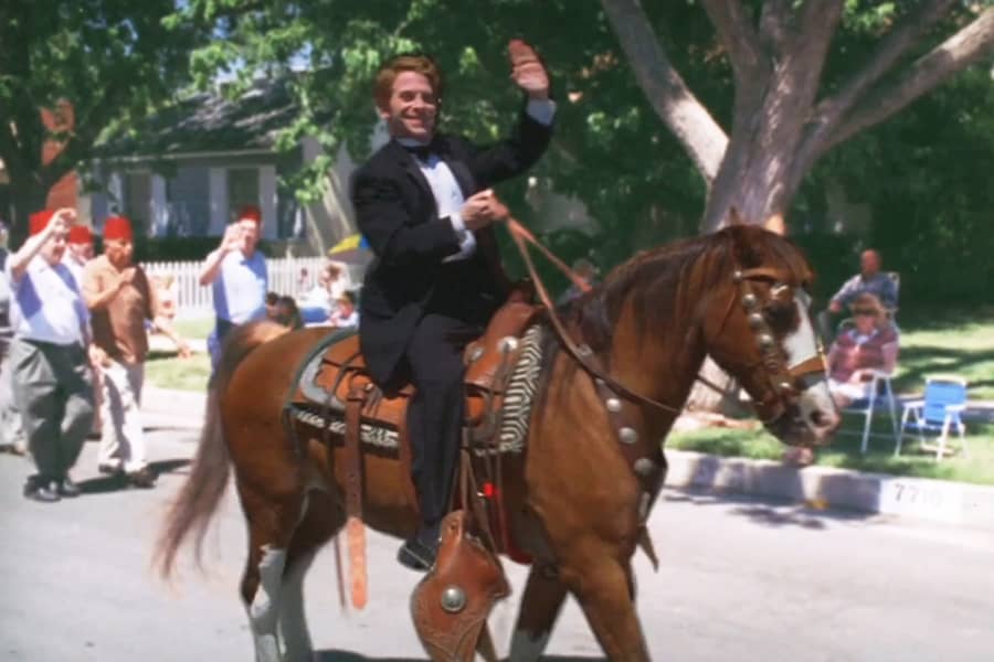 Buddy Zaks waves while riding a horse down the street