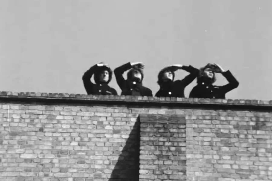 the Rutles on a building’s roof, shading their faces with their hands