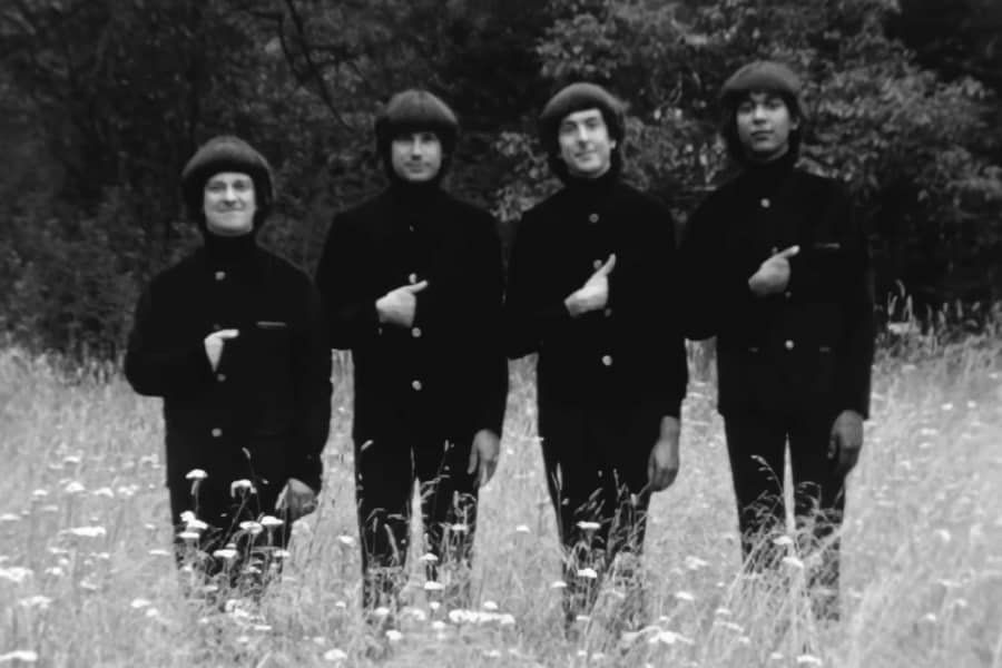 the Rutles all in black, in a field, with their hands tucked into their shirts
