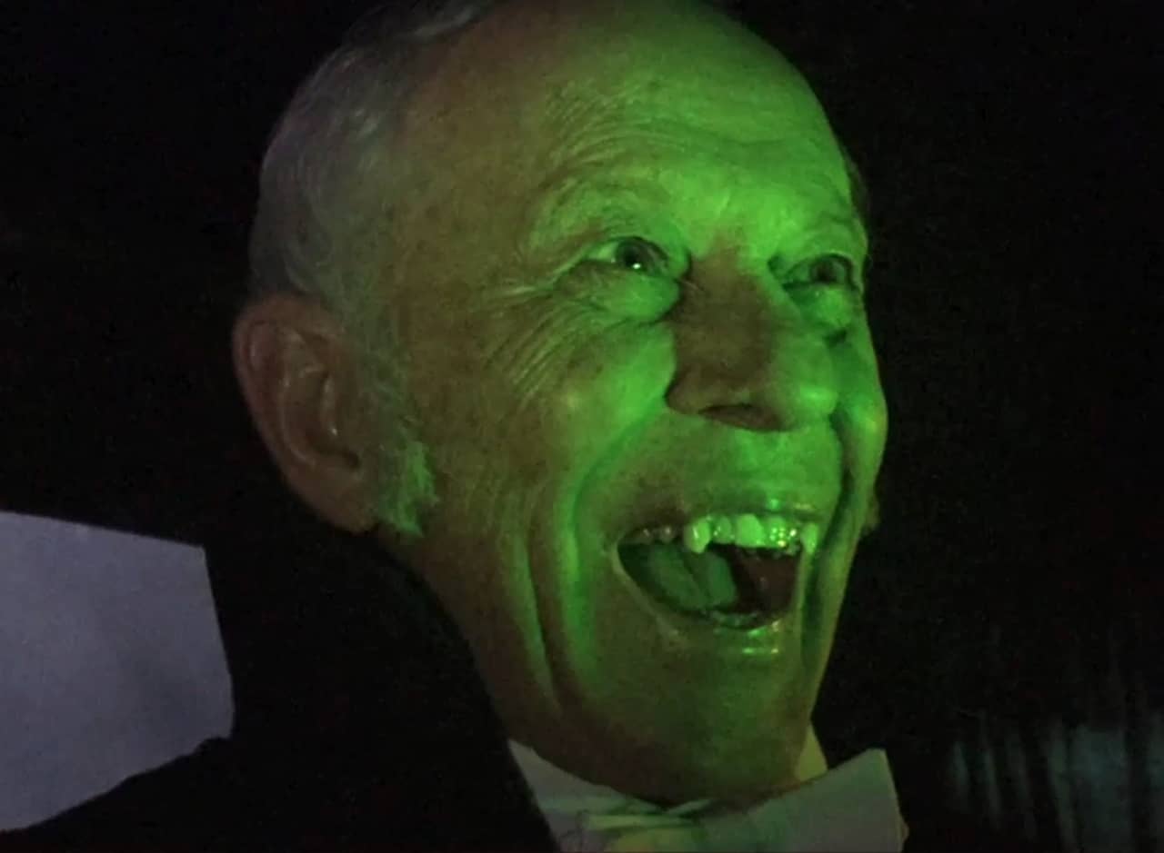old man glowing green and smiling with sharp vampire teeth