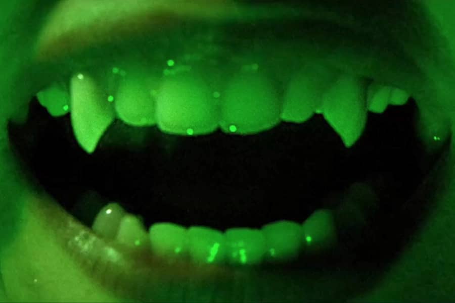 close-up of glowing green smile with vampire teeth