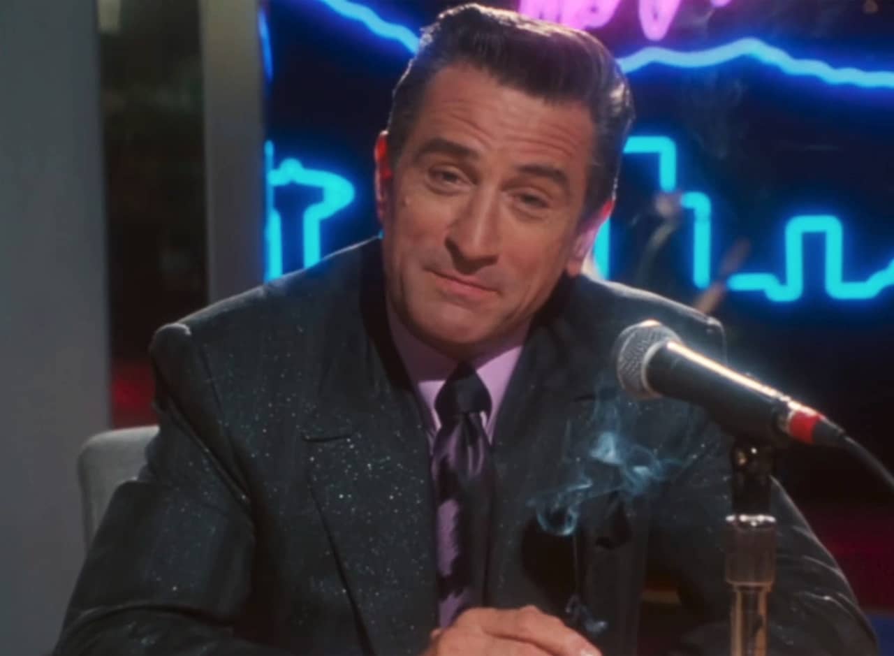 Sam Rothstein, in a suit and smoking in front of a microphone