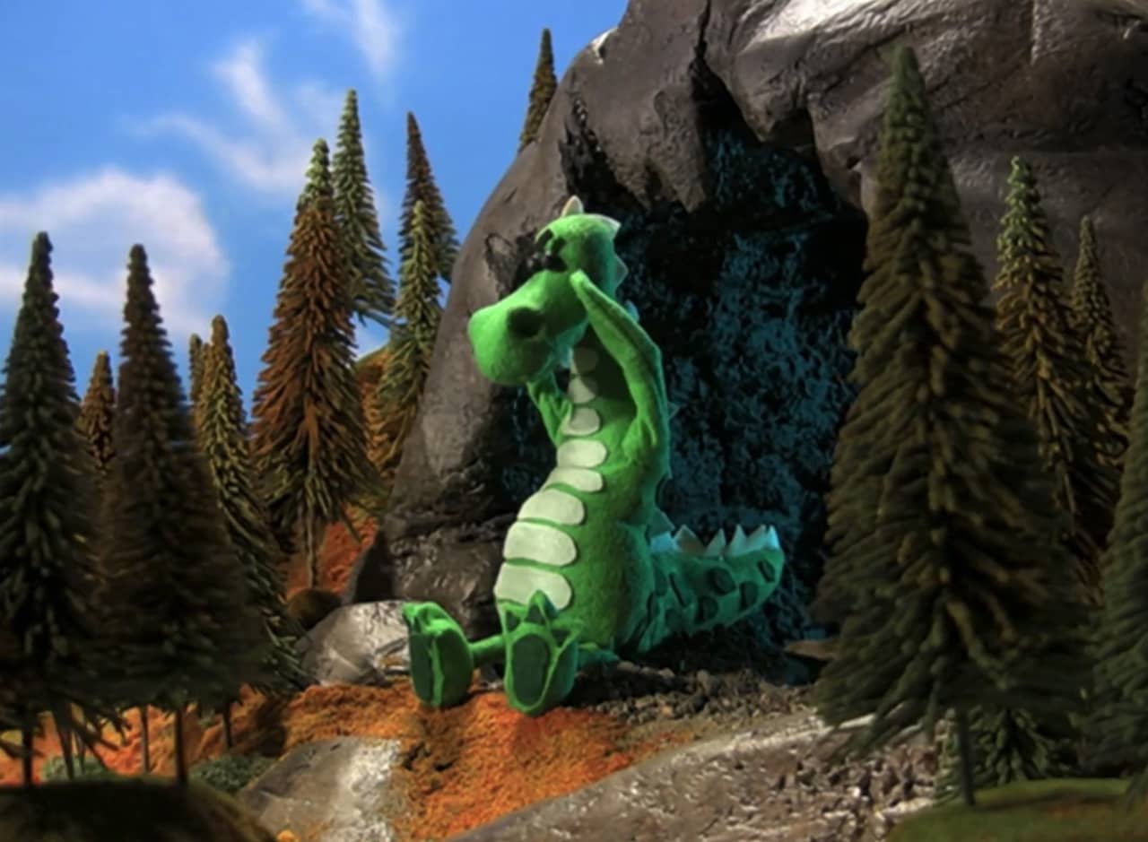 Albi, a sad felt dragon, sits outside a cave