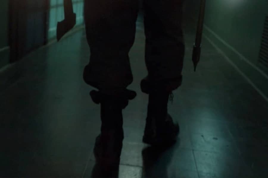 Hatchet Man’s feet as he walks down a dark hallway, weilding an axe in each hand