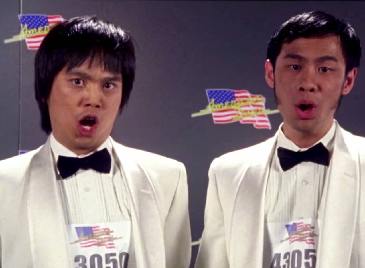 two awkward men in white tuxedos sing a duet