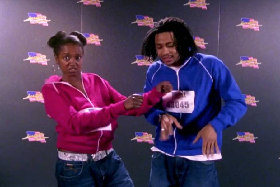 a man and woman in matching track jackets sing and dance