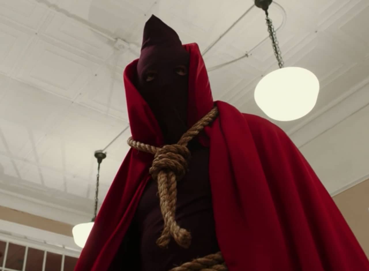 Hooded Justice, a masked man wearing a high-collared, red cape and noose around his neck