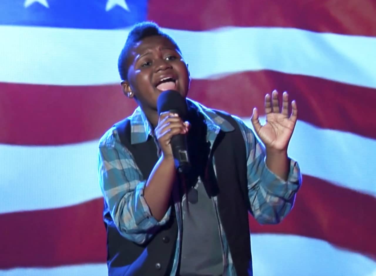 a young boy sings in front of an American flag backdrop