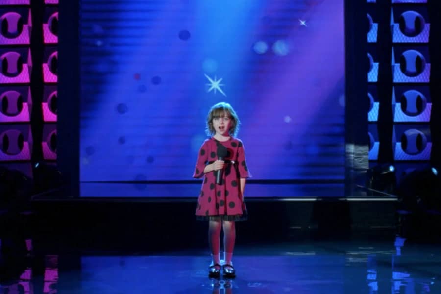 a young girl looks tiny singing on a giant stage