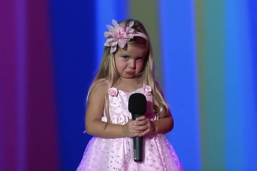 a young girl in an adorable dress holds a microphone and looks dejected