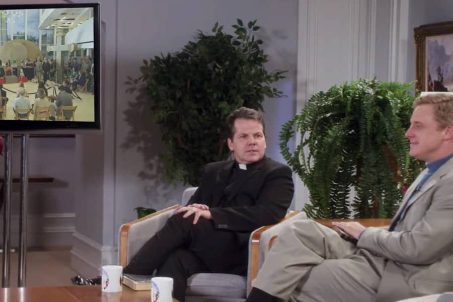 the pastor and priest chat while viewing a nearby tv