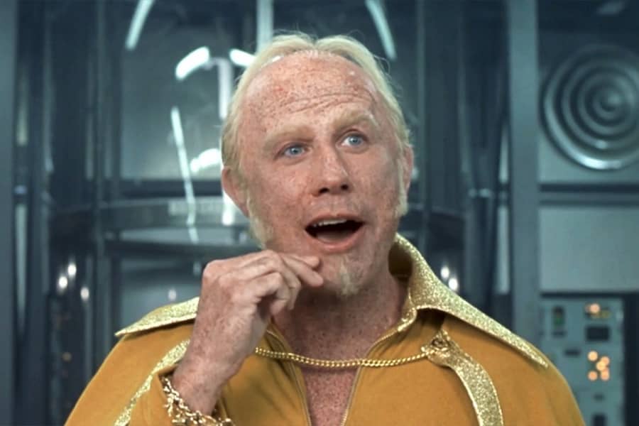 John Travolta dressed as Goldmember picks at his chin skin