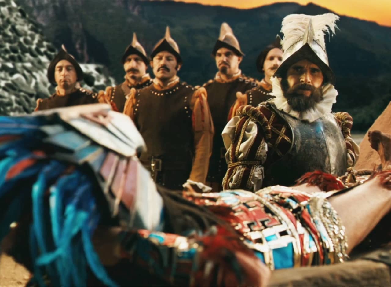 a man in colorful Aztec clothing, tied down by Spanish conquistadors