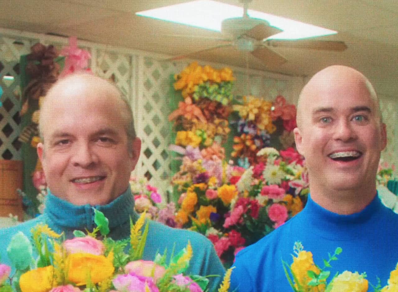 Mr. Steve and Mr. Mike, two bald men in blue turtlenecks, holding flowers