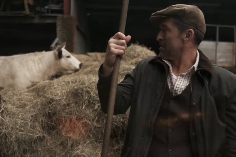 Detective sits next to a cow in the stable