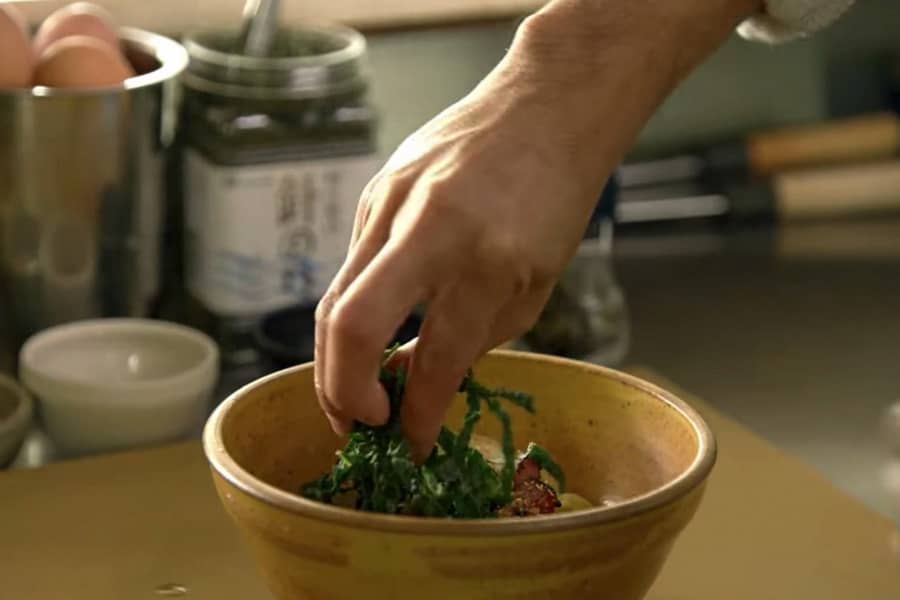 a hand delicately dresses a bowl of ramen