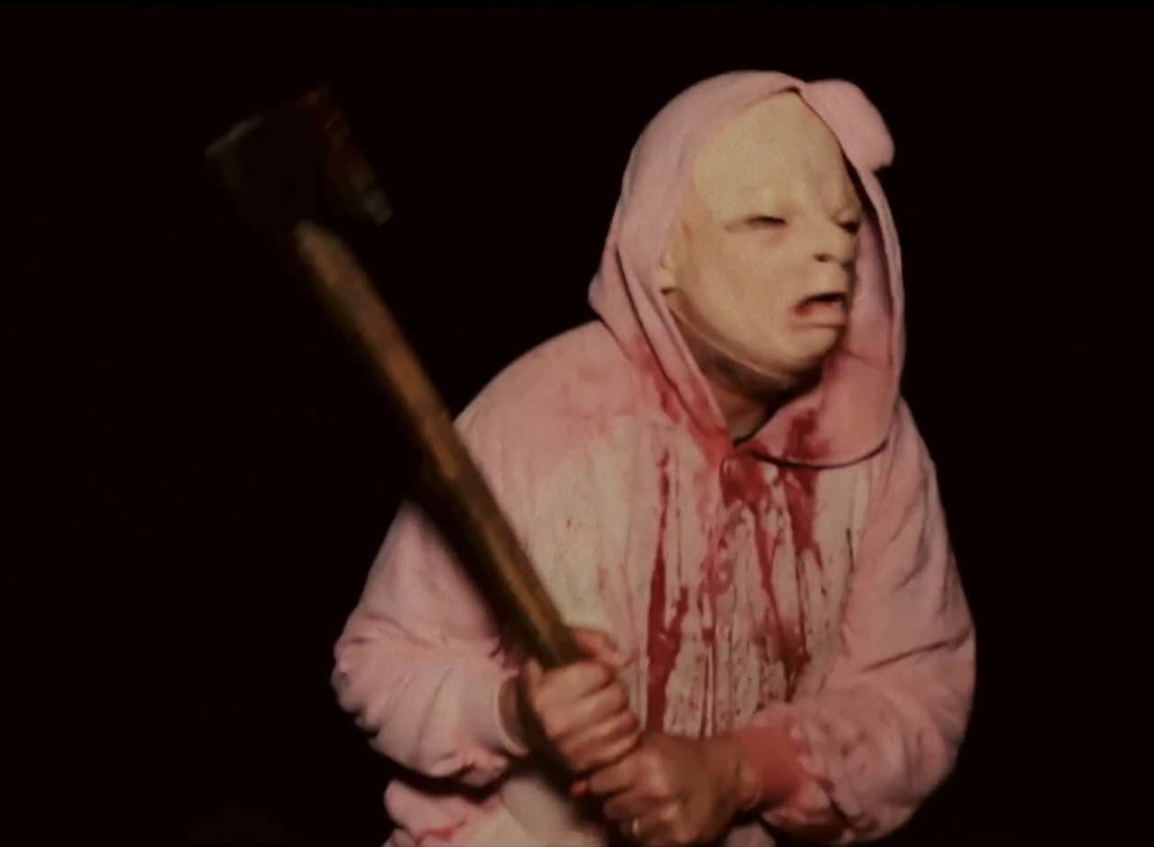 a man in a pink jumper covered in blood wears a baby face mask holds an axe