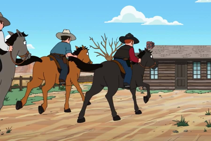 cowboys on horses run toward a building