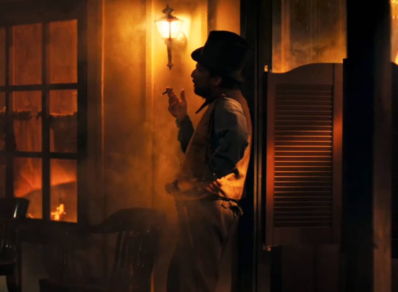 Billy the Kid smoking a cigarette in front of a burning house