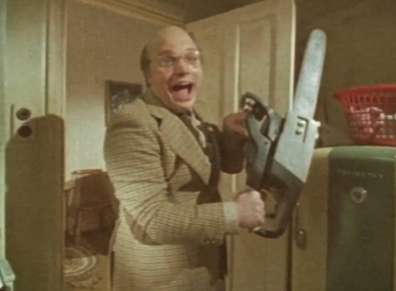 Randolph Caer as Sidney King holding up a chainsaw and smiling