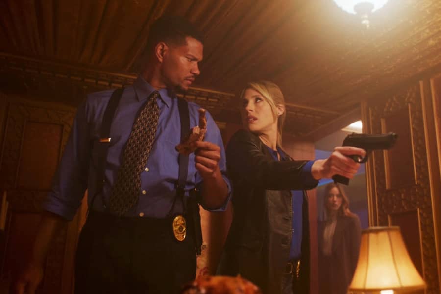 Turner holds an animal bone and Green holds a gun while they look at each other