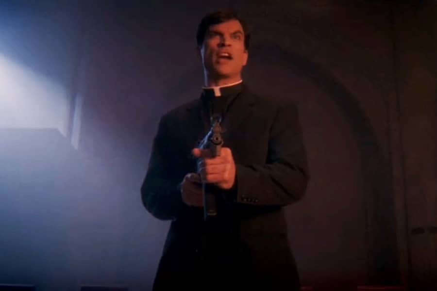 Sean Walker as the priest holding a gun