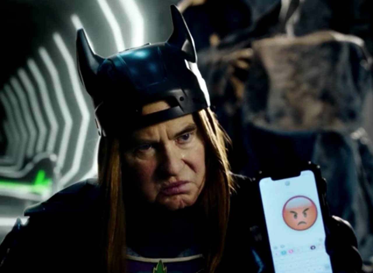Val Kilmer as Bluntman holding up an iPhone with an angry emoji
