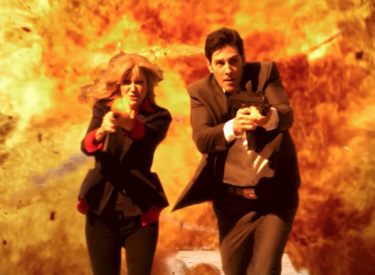 a man and woman team (Lister and Reichs) firing guns as they run away from a huge explosion