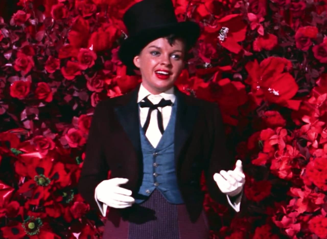 a woman in a fancy suit sings in front of a wall of roses
