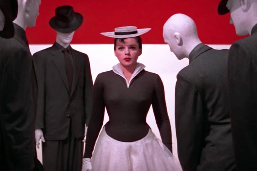 the woman stands in a tight space with well-dressed mannequins