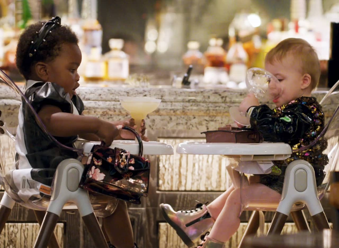 two babies in fancy outfits drinking cocktails