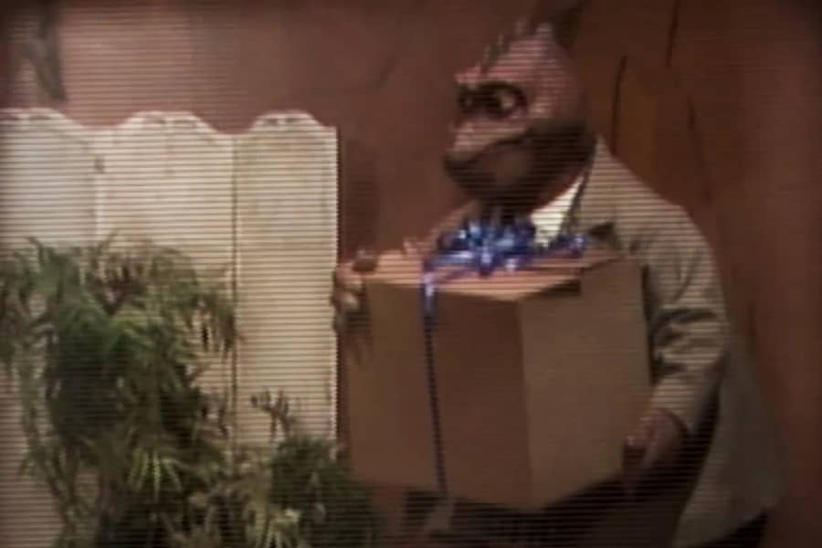 man dinosaur walking in with a cardboard box with a ribbon on it