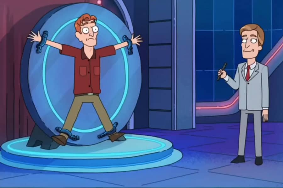 host stands near a guy who is strapped down to a vertical, circular wheel
