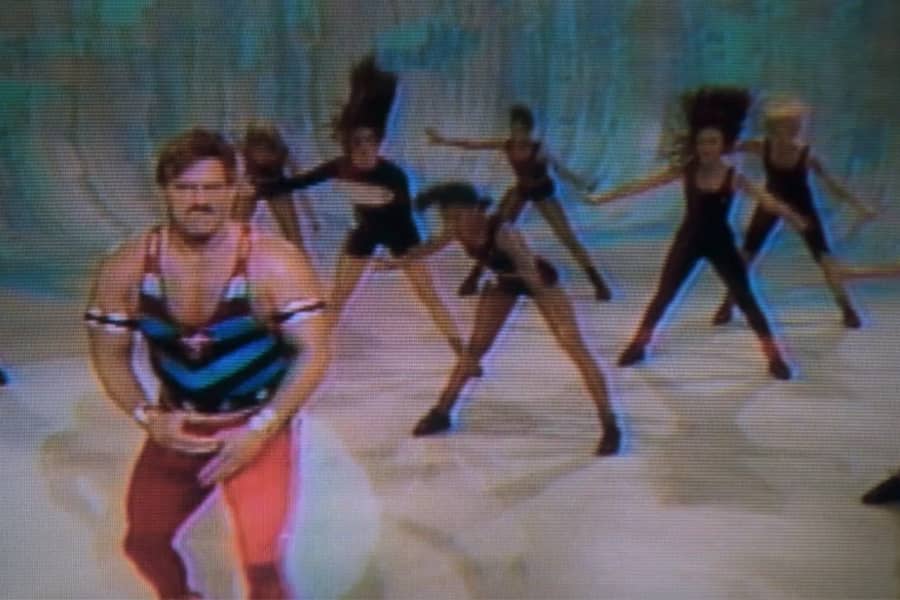 Captain Freedom flexing with women exercising behind him