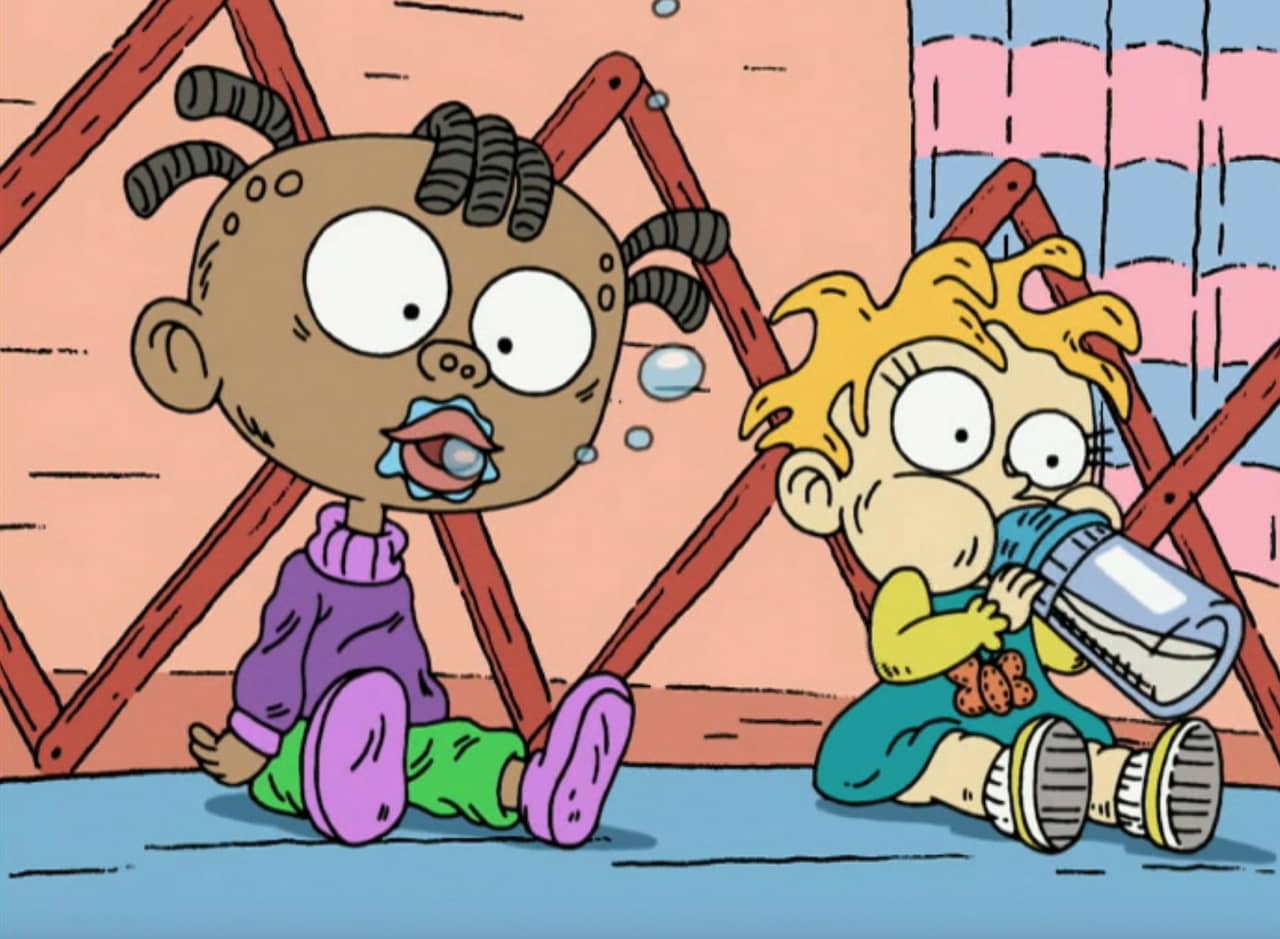 two babies in a pen, one drinking a bottle and one blowing spit bubbles