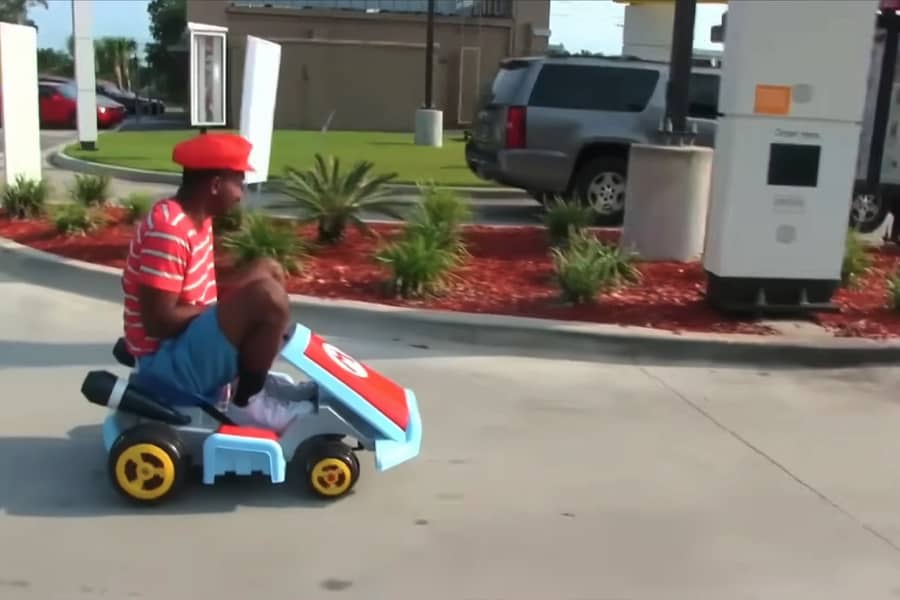 Charley wearing a Mario hat and driving a Mario Kart to a drive-thru